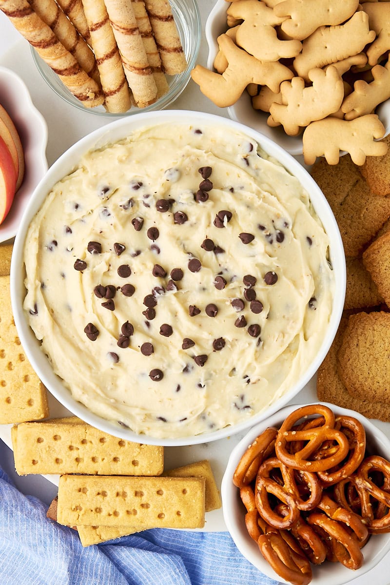 overhead view of cookie dough dip in a white bowl with cookies, pretzels, and more dippers surrounding