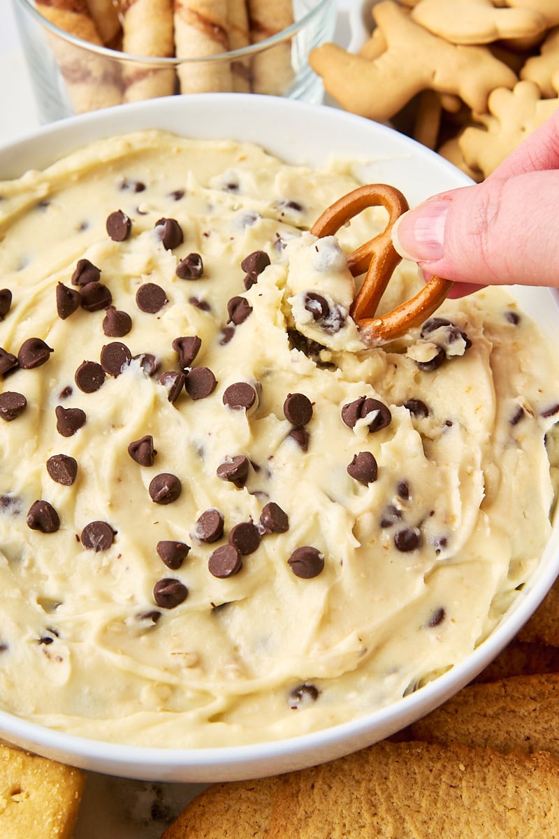 a pretzel being dipped into a bowl of cookie dough dip