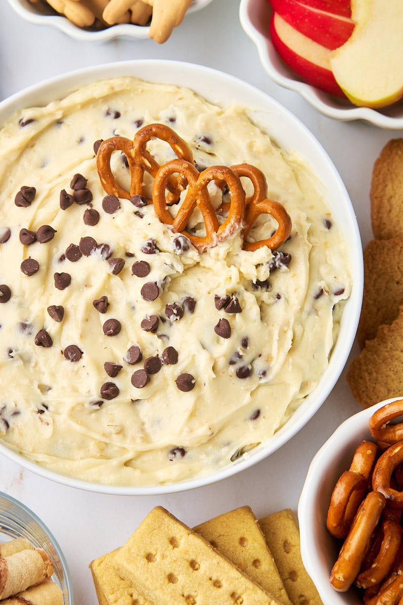 overhead view of cookie dough dip in a white bowl surrounded by pretzels, apple slices, and other dippers