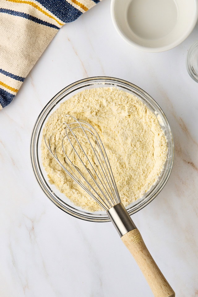 overhead view of flour, cornmeal, baking powder, and salt whisked together in a glass mixing bowl