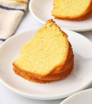 a slice of cornmeal pound cake on a white plate with another slice in the background