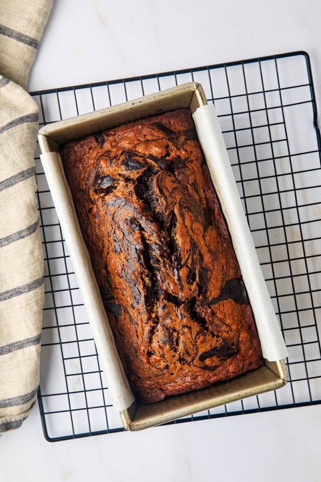 overhead view of freshly baked marbled chocolate banana bread in a loaf pan on a wire rack