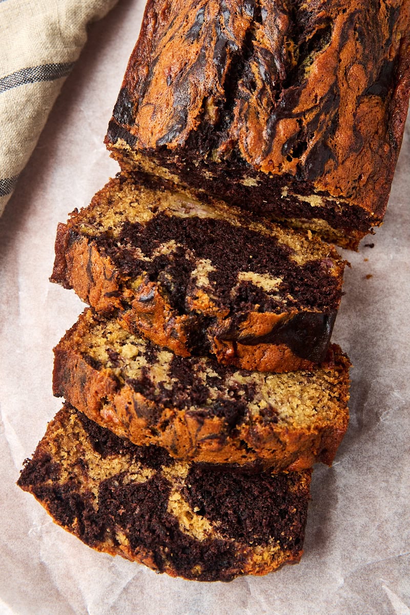 overhead view of partially sliced marbled chocolate banana bread on parchment paper