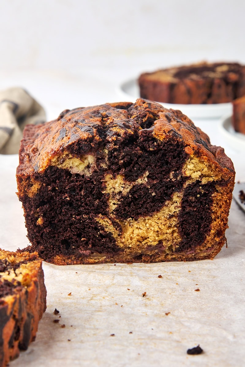 part of a loaf of marbled chocolate banana bread on parchment paper with more bread partially visible surrounding
