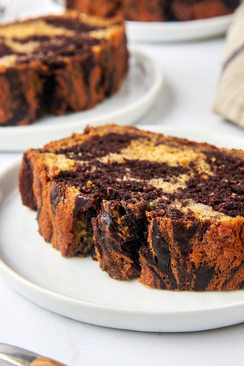 a slice of marbled chocolate banana bread on a white plate with more slices of bread in the background