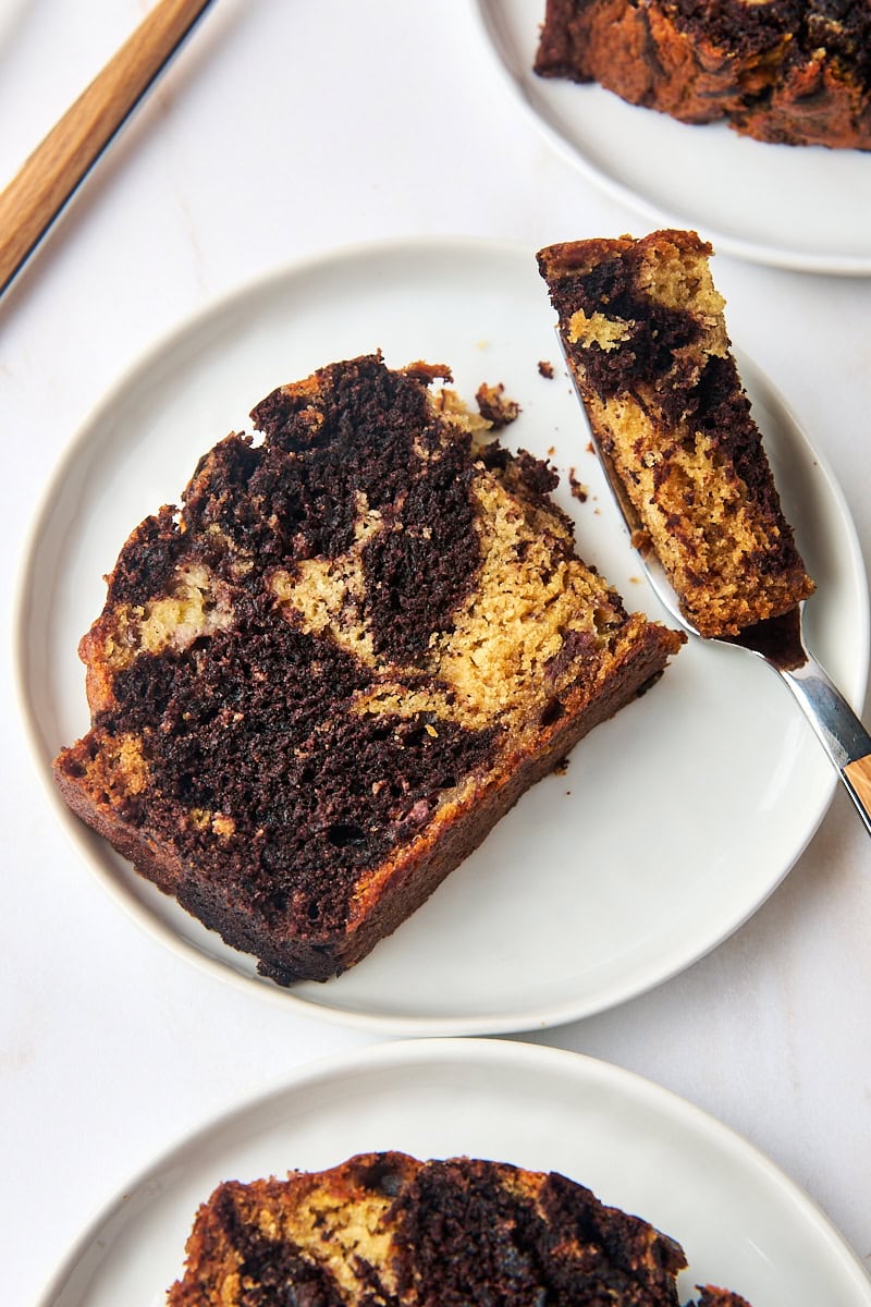 a slice of marbled chocolate banana bread on a white plate with a bite on a fork