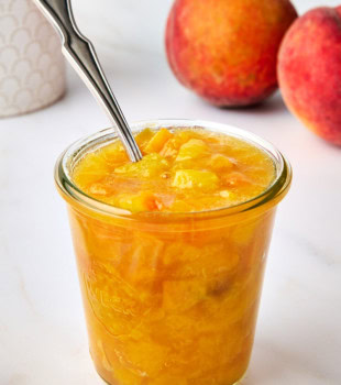 peach compote in a glass jar with a spoon resting inside