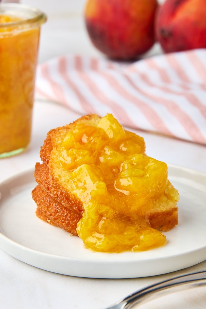 peach compote spooned over a slice of pound cake on a white plate