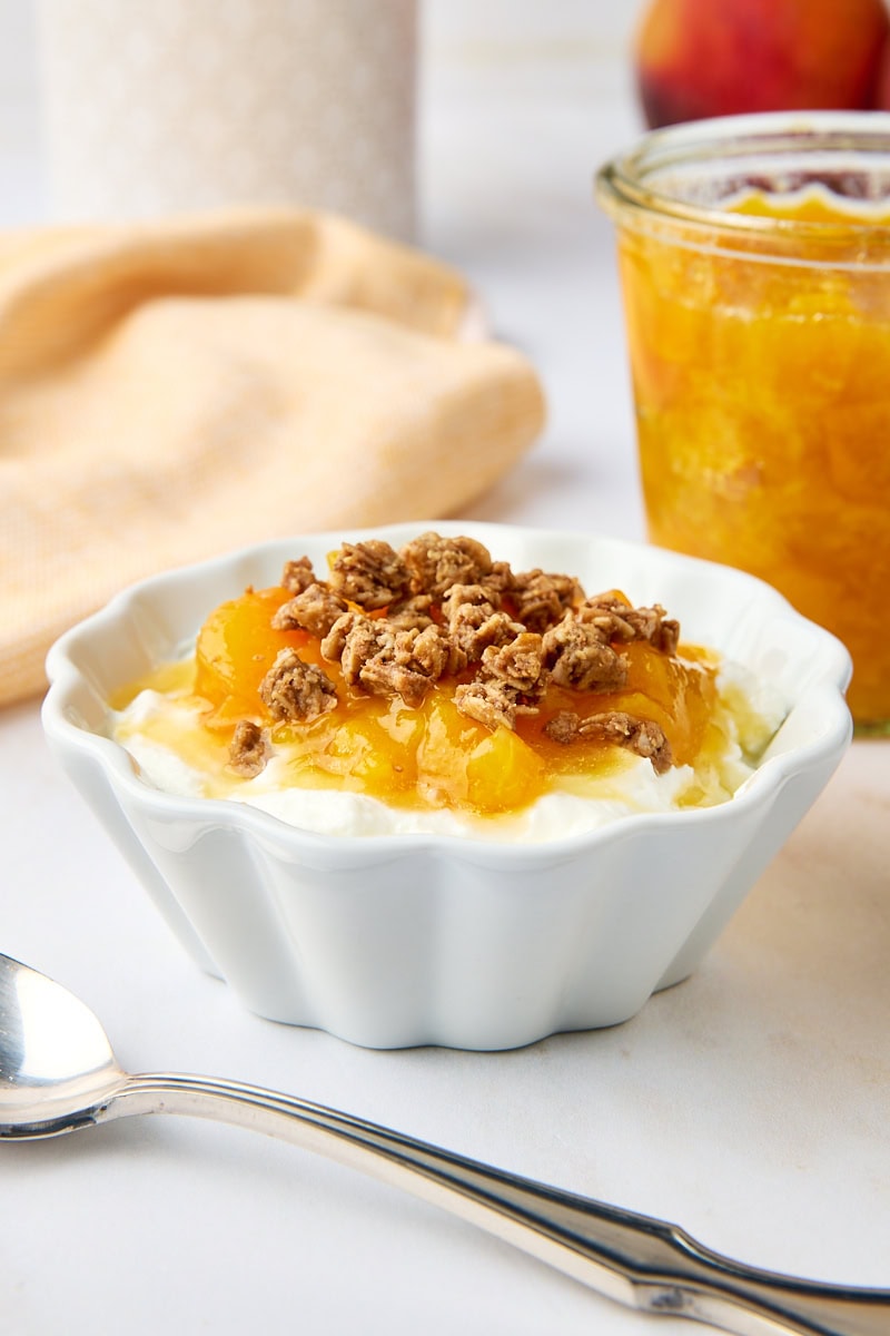 peach compote and granola over yogurt in a white bowl