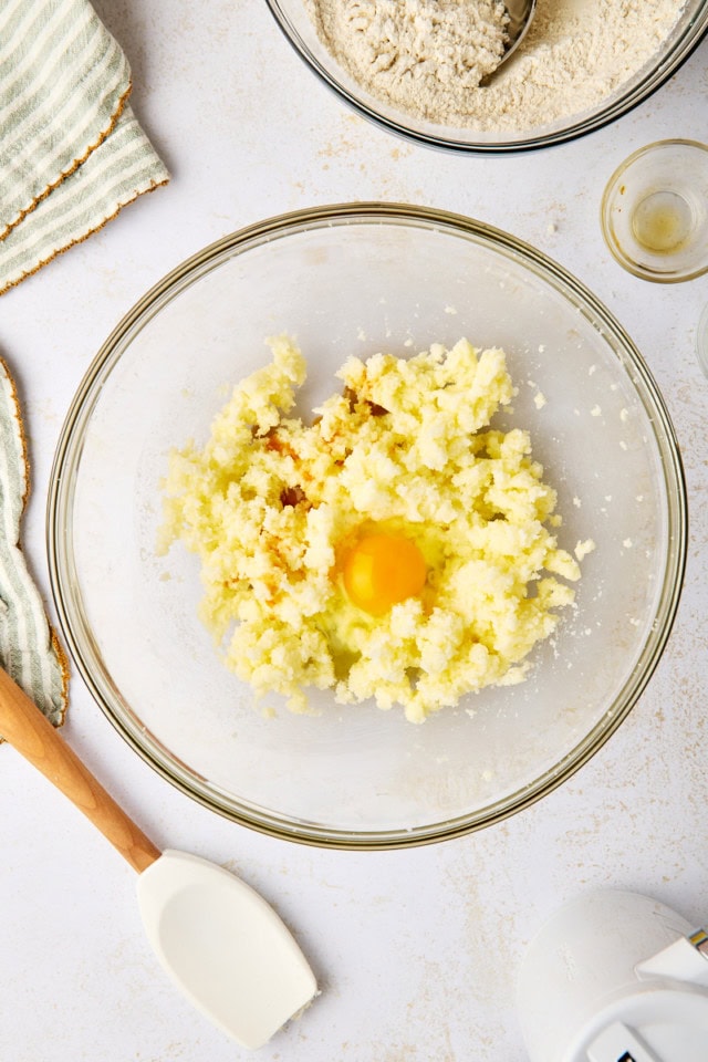 overhead view of egg , almond extract, and vanilla extract added to creamed butter and sugar in a glass mixing bowl