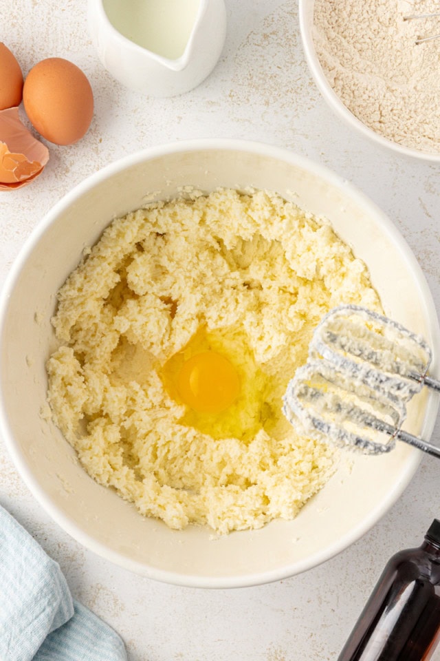 overhead view of egg added to creamed butter and sugar in a white mixing bowl