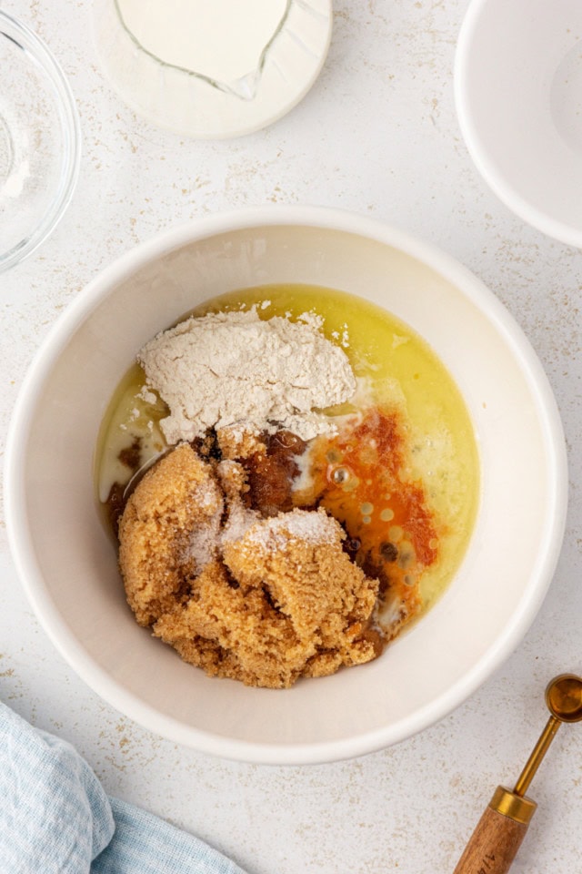 overhead view of brown sugar, melted butter, flour, milk, salt, and vanilla in a white mixing bowl