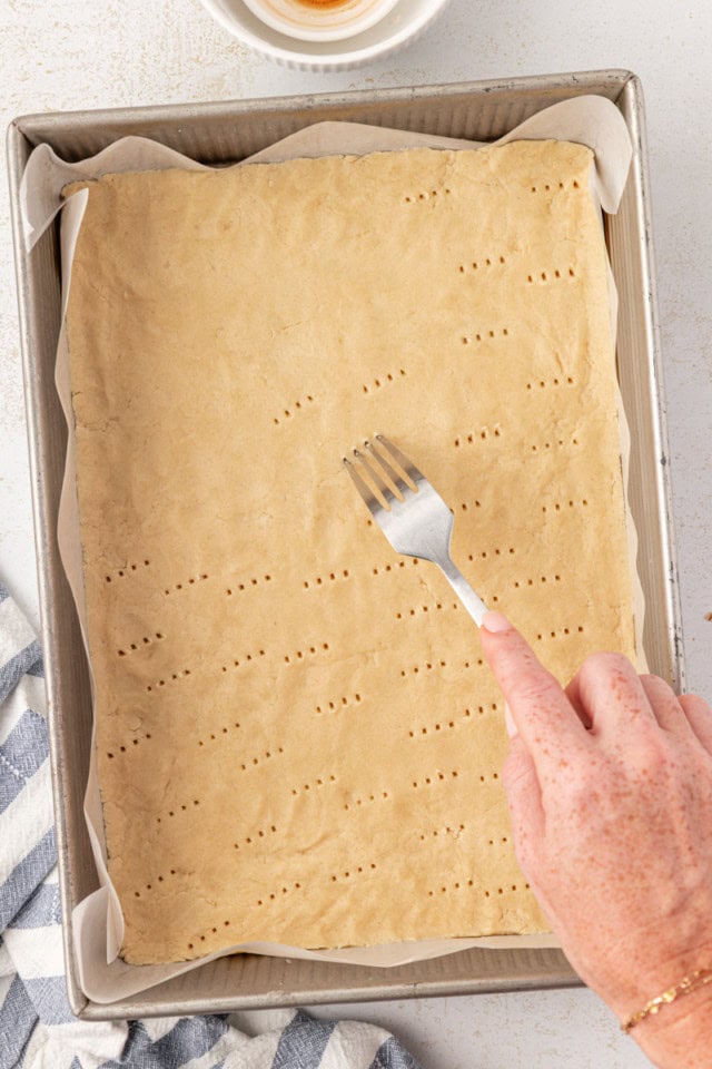 overhead view of shortbread crust being docked with a fork in a 9x13 pan