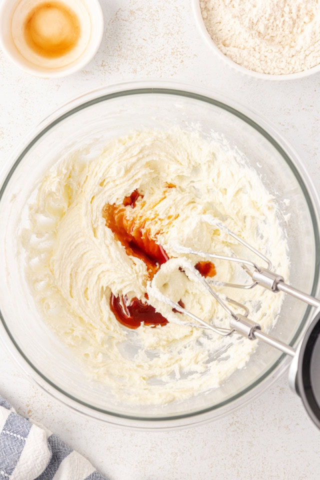 overhead view of vanilla extract added to creamed butter and sugar in a glass mixing bowl