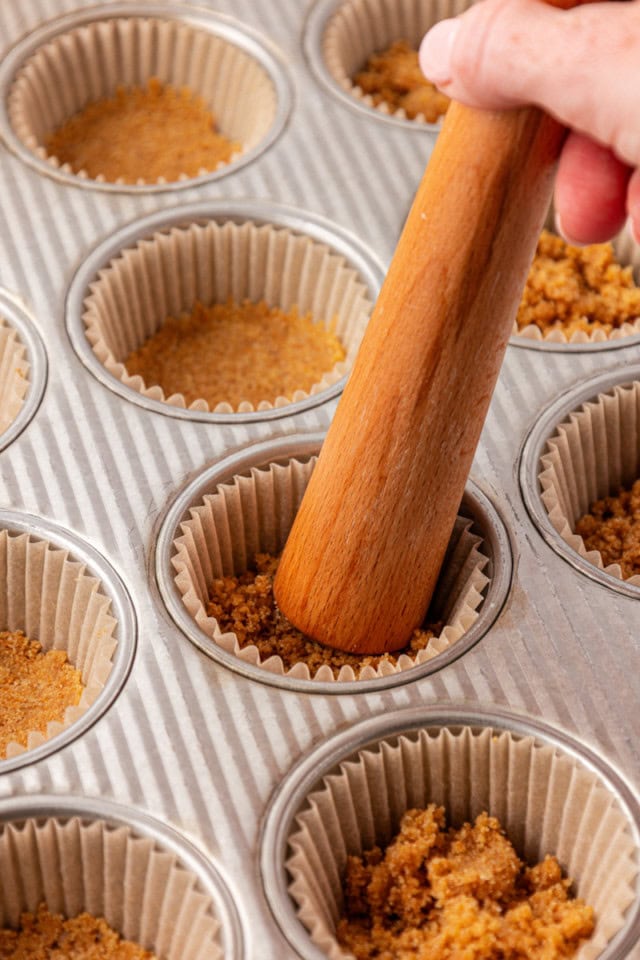 graham cracker crust being pressed into lined muffin pans