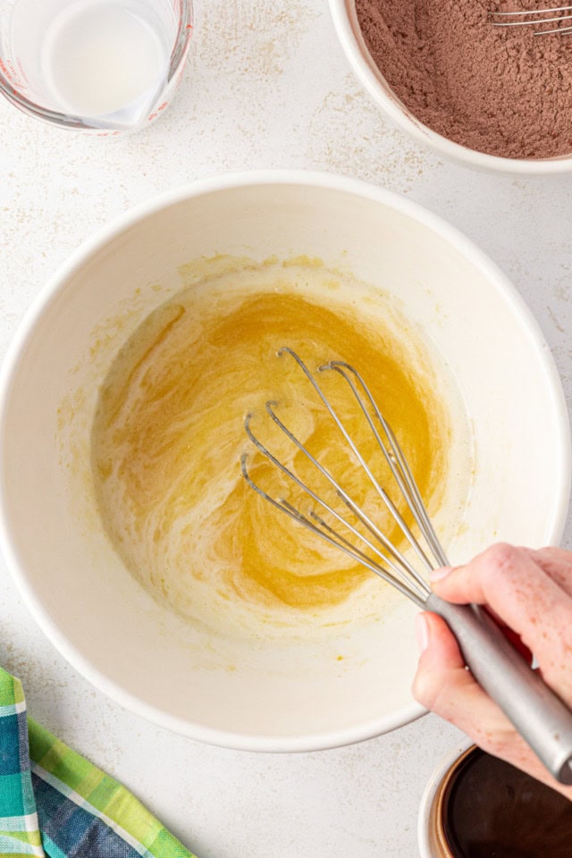 overhead view of melted butter, sugar, eggs, and vanilla being whisked together in a white bowl