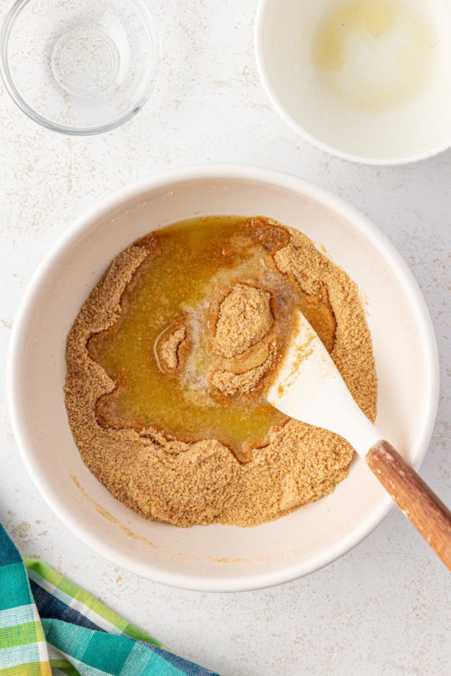 graham cracker crust ingredients being mixed together in a white bowl