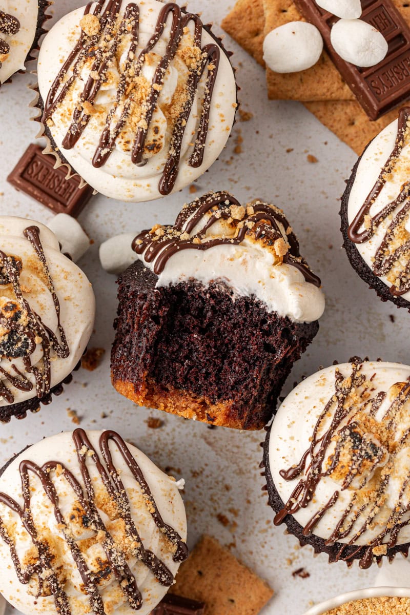 overhead view of a s'mores cupcake turned on its side with a bite missing surrounded by more cupcakes