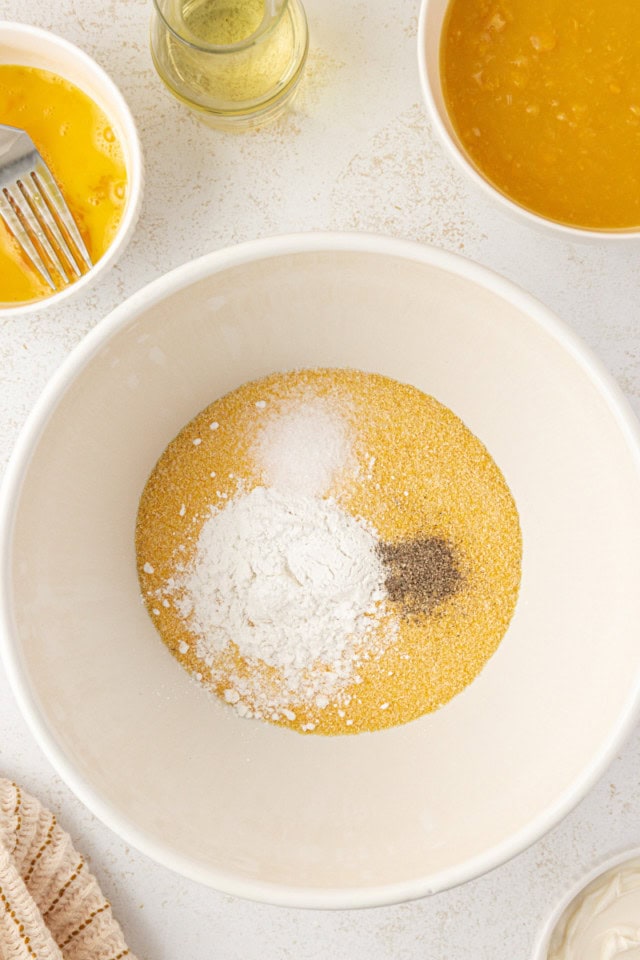 overhead view of cornmeal, baking powder, salt, and pepper in a white mixing bowl
