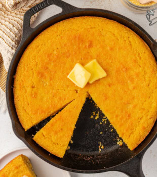 sour cream corn bread topped with two pats of butter in a cast iron skillet
