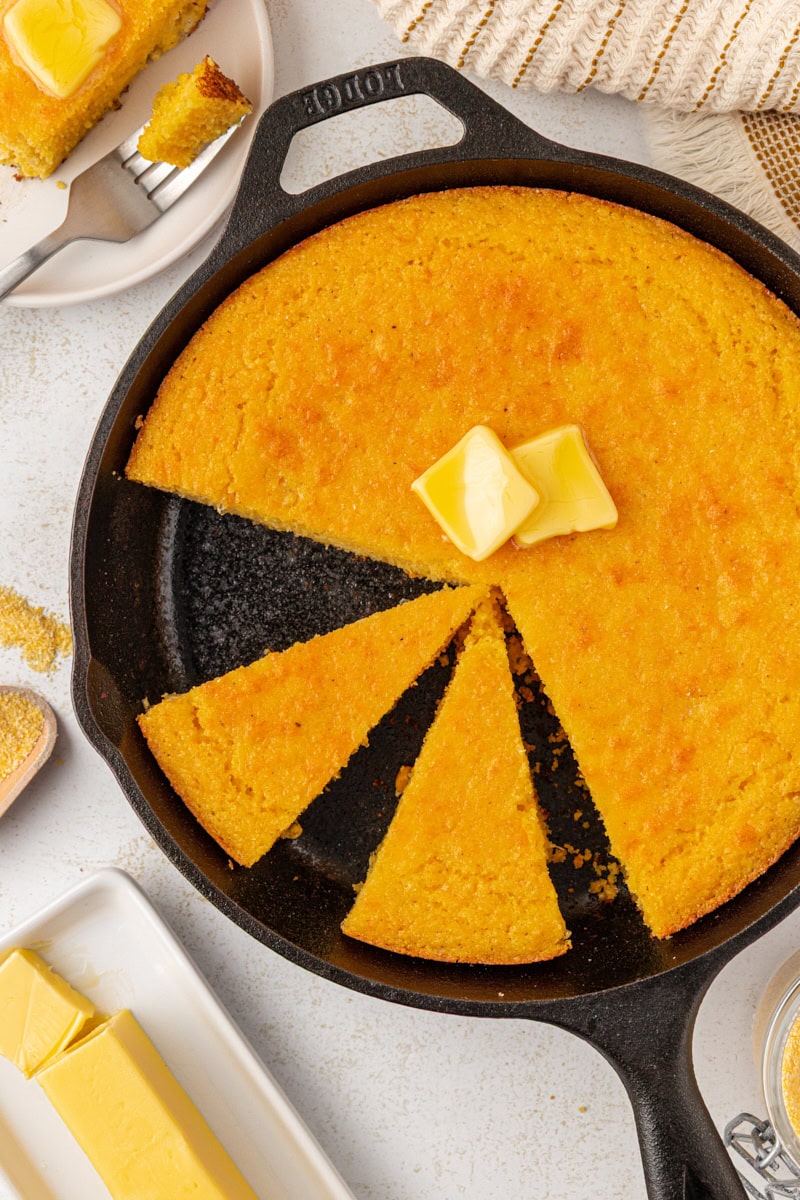 overhead view of two slices of sour cream corn bread in a cast iron skillet with the remaining corn bread