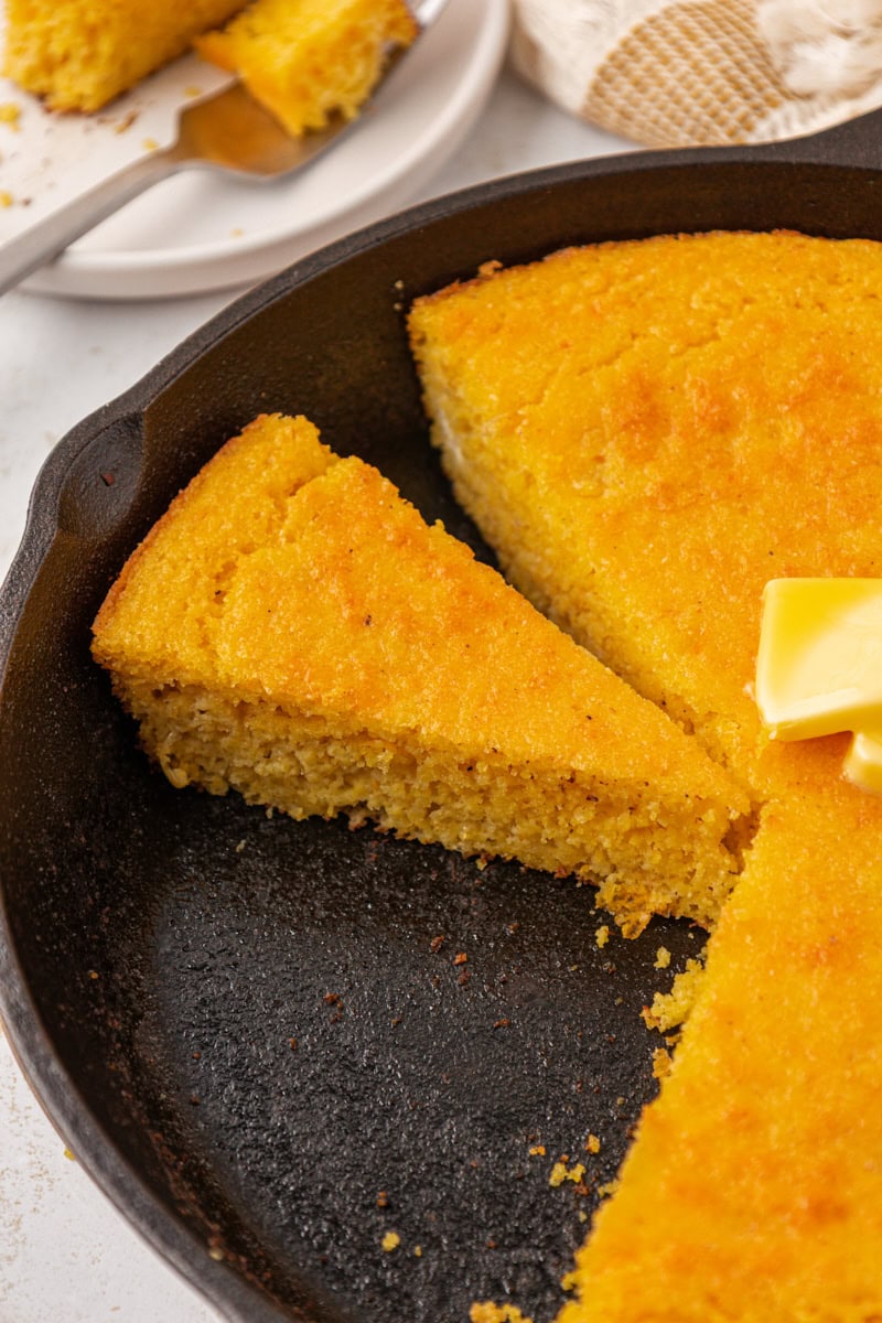 a slice of sour cream corn bread alongside more unsliced corn bread in a cast iron skillet