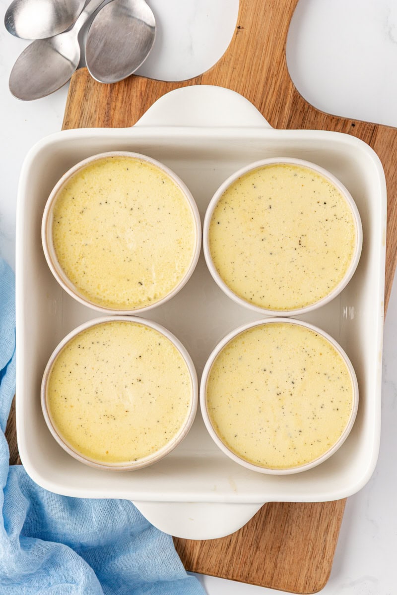 overhead view of freshly baked vanilla bean pots de crème in ramekins inside a white baking dish