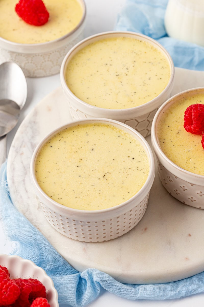 three vanilla bean pots de crème on a marble serving tray with another serving in the background