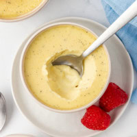 overhead view of a vanilla bean pots de crème with a spoon resting inside, set on a white plate with two fresh raspberries