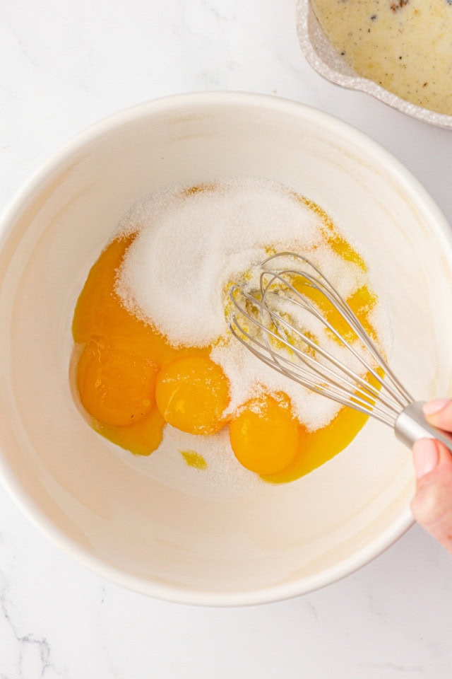 overhead view of egg yolks, sugar, and salt being whisked together in a white mixing bowl