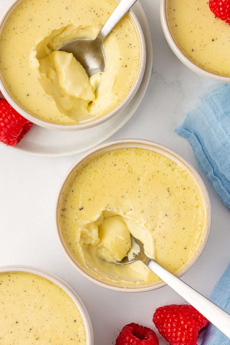 two vanilla bean pots de crème with spoons resting where bites are missing