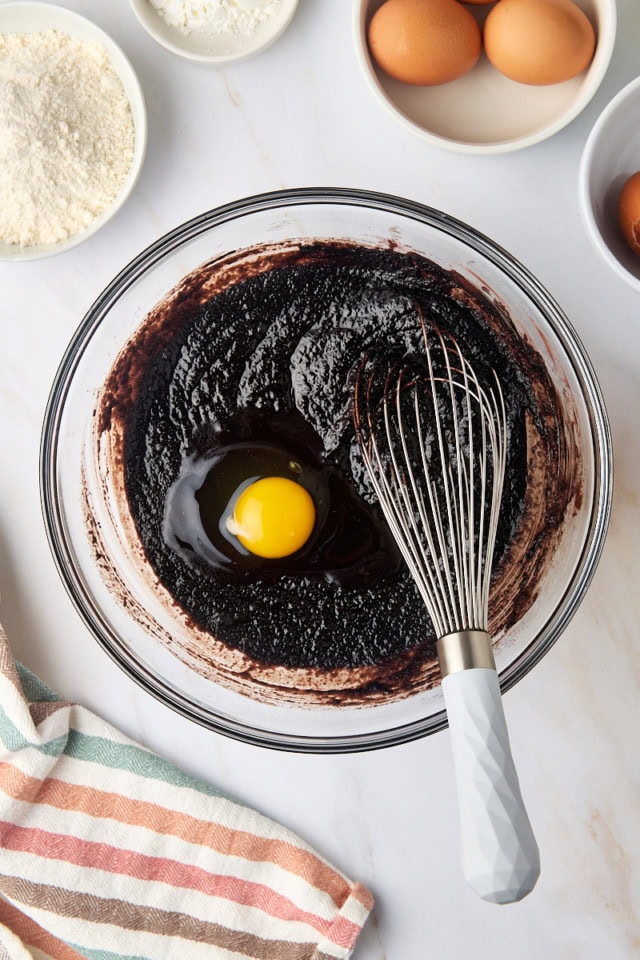 overhead view of egg added to brownie batter in a glass mixing bowl
