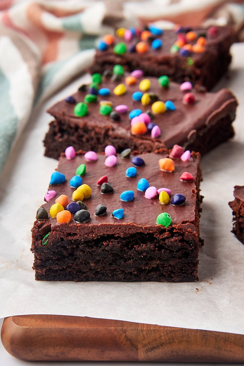 three cosmic brownies lined up on a parchment-covered wooden cutting board