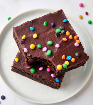 stack of two cosmic brownies on a white plate with a bite missing from the top brownie