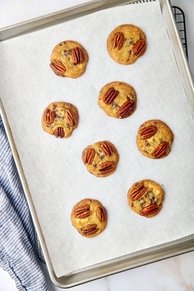 overhead view of freshly baked triple chocolate pecan cookies on a parchment-lined baking sheet