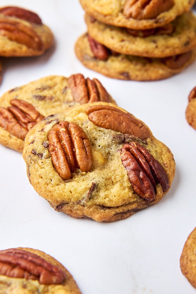 two triple chocolate pecan cookies on a white surface with more cookies surrounding