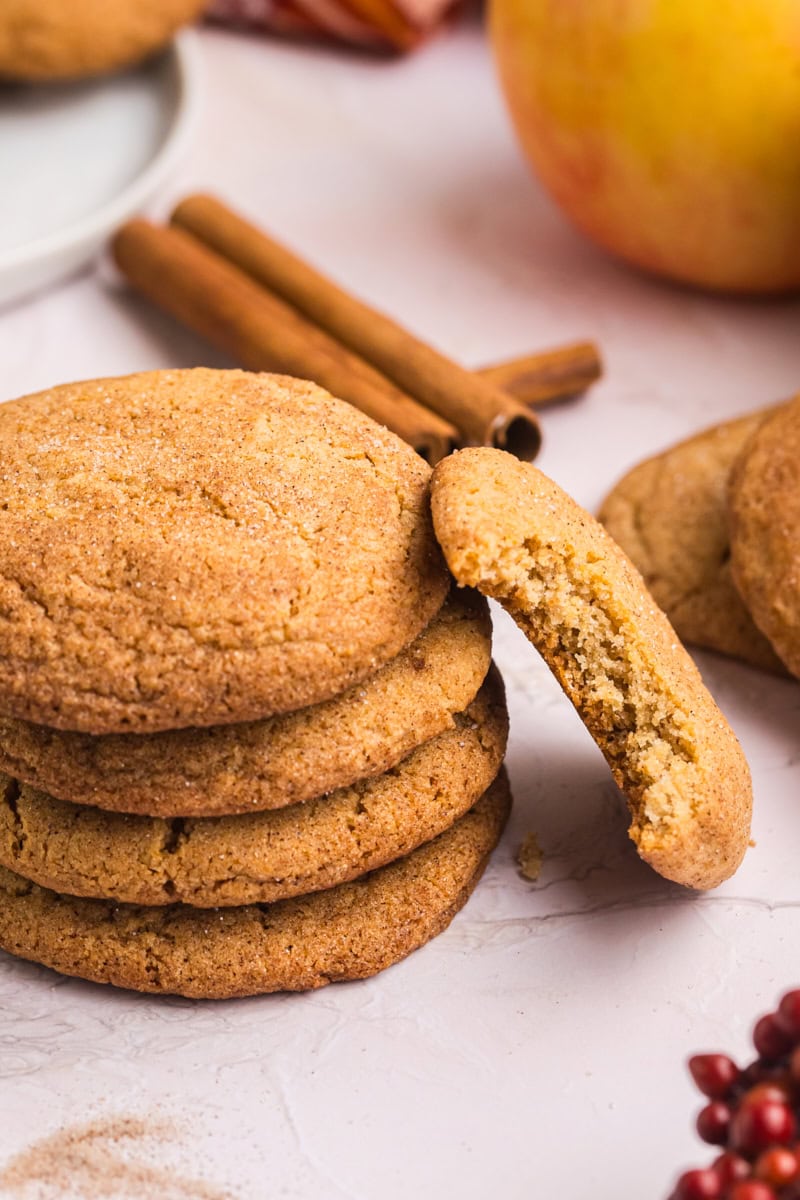 an apple butter snickerdoodle with a bite missing leaning against a stack of four more cookies