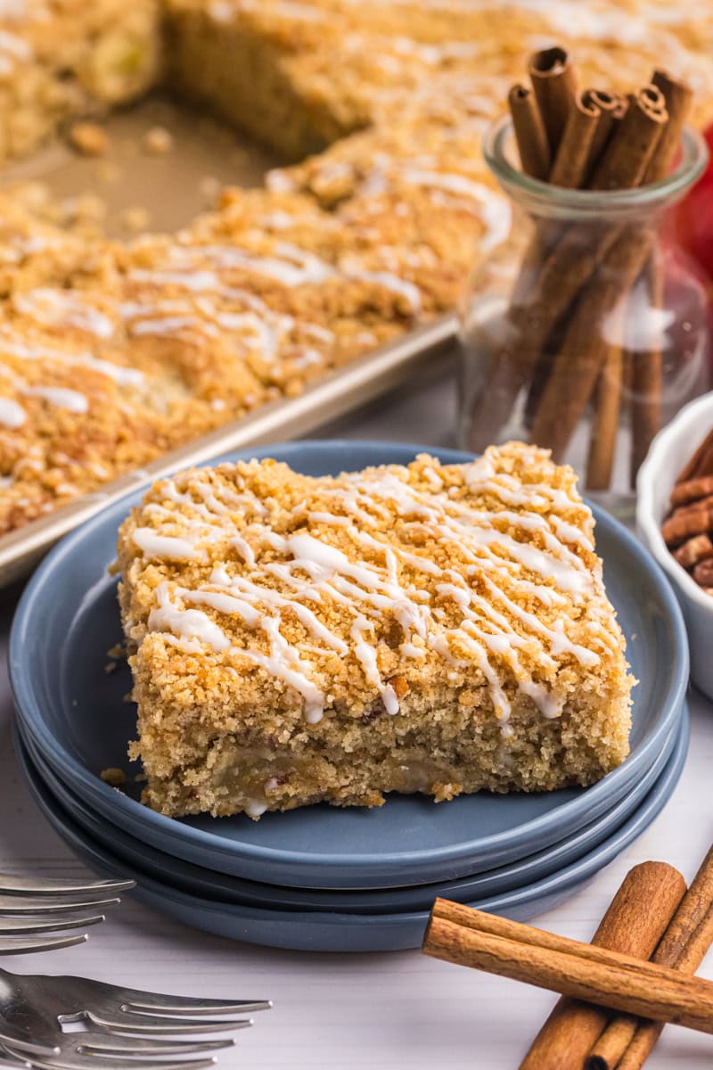a slice of apple crumb sheet cake on a blue plate with the remaining cake in a half sheet pan in the background