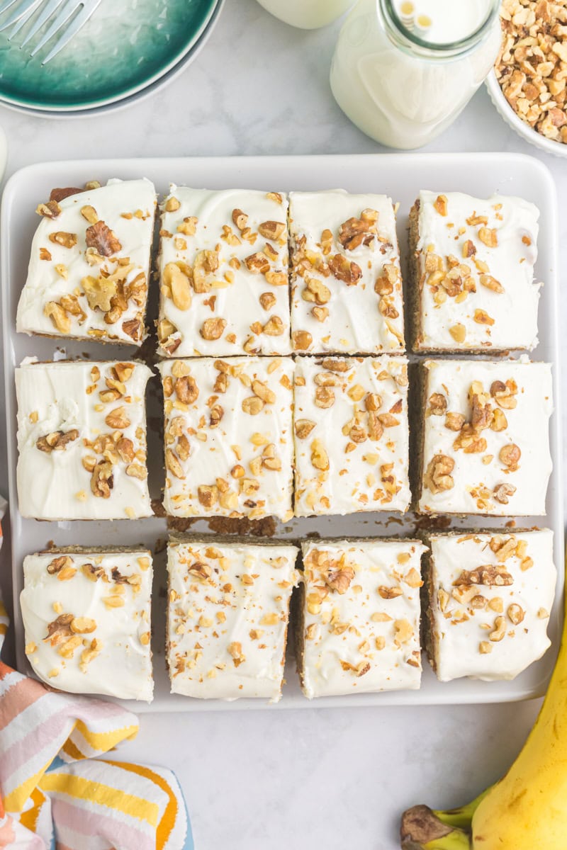 overhead view of sliced banana cake with cream cheese frosting on a square white serving plate