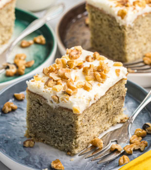 a slice of banana cake with cream cheese frosting on a blue plate with more servings in the background