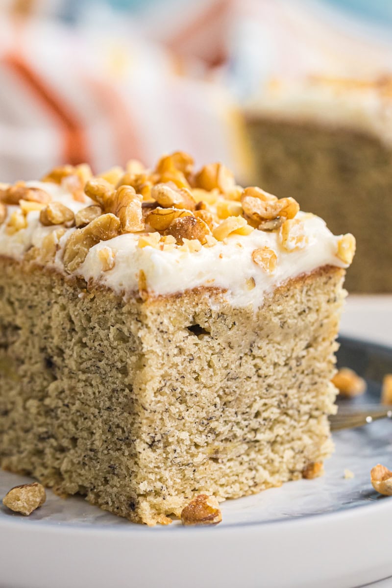 close-up of a slice of banana cake with cream cheese frosting topped with toasted chopped nuts