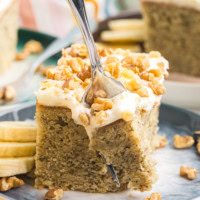 a fork cutting into a slice of banana cake with cream cheese frosting