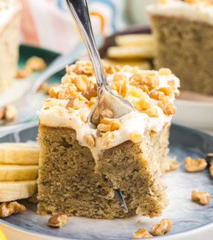 a fork cutting into a slice of banana cake with cream cheese frosting