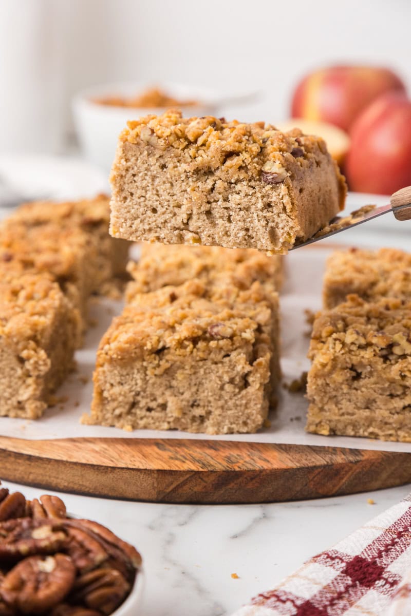 a slice of caramel apple crumb cake on a cake server with the remaining cake in the background