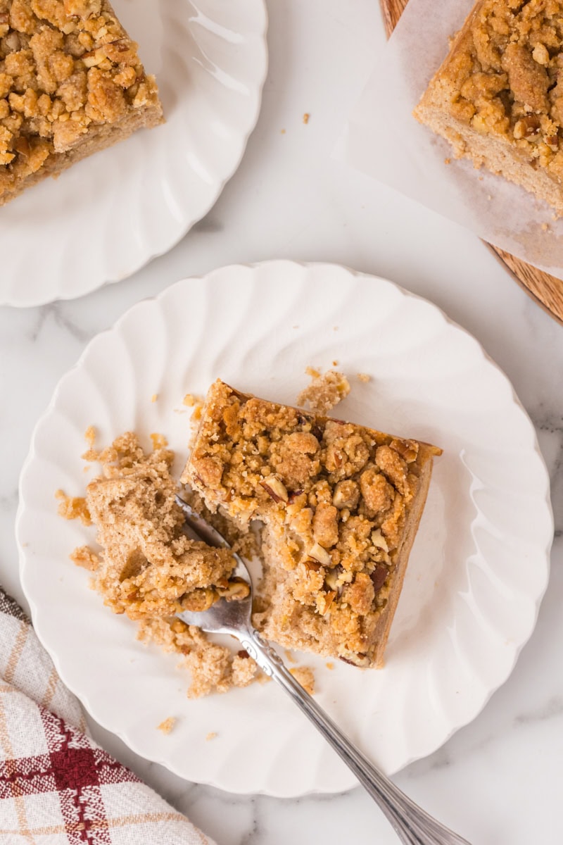 overhead view of a slice of caramel apple crumb cake on a white plate with a bite on a fork