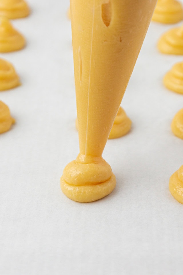 choux pastry dough being piped onto a parchment-lined baking sheet