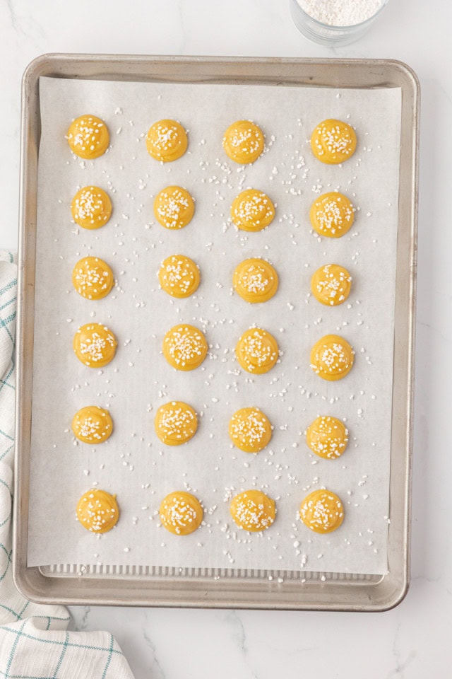 overhead view of chouquettes piped onto a parchment-lined baking sheet and topped with pearl sugar, ready to go into the oven