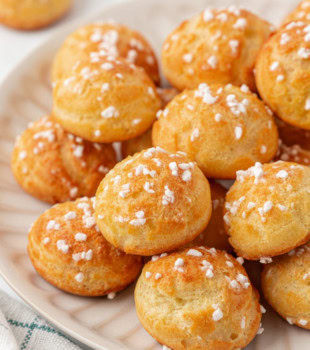golden chouquettes topped with pearl sugar, stacked on a white plate