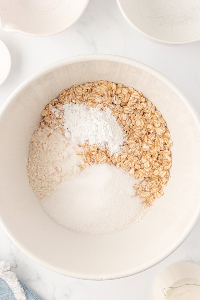 overhead view of flour, oat, sugar, baking powder, and salt in a white mixing bowl