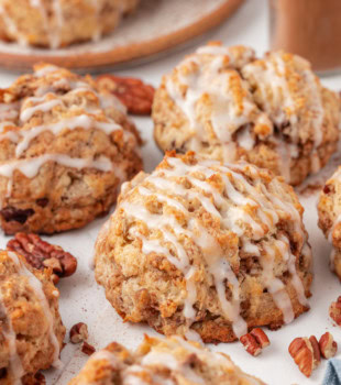 several cinnamon bun scones on a white surface with a plate of scones partially visible in the background